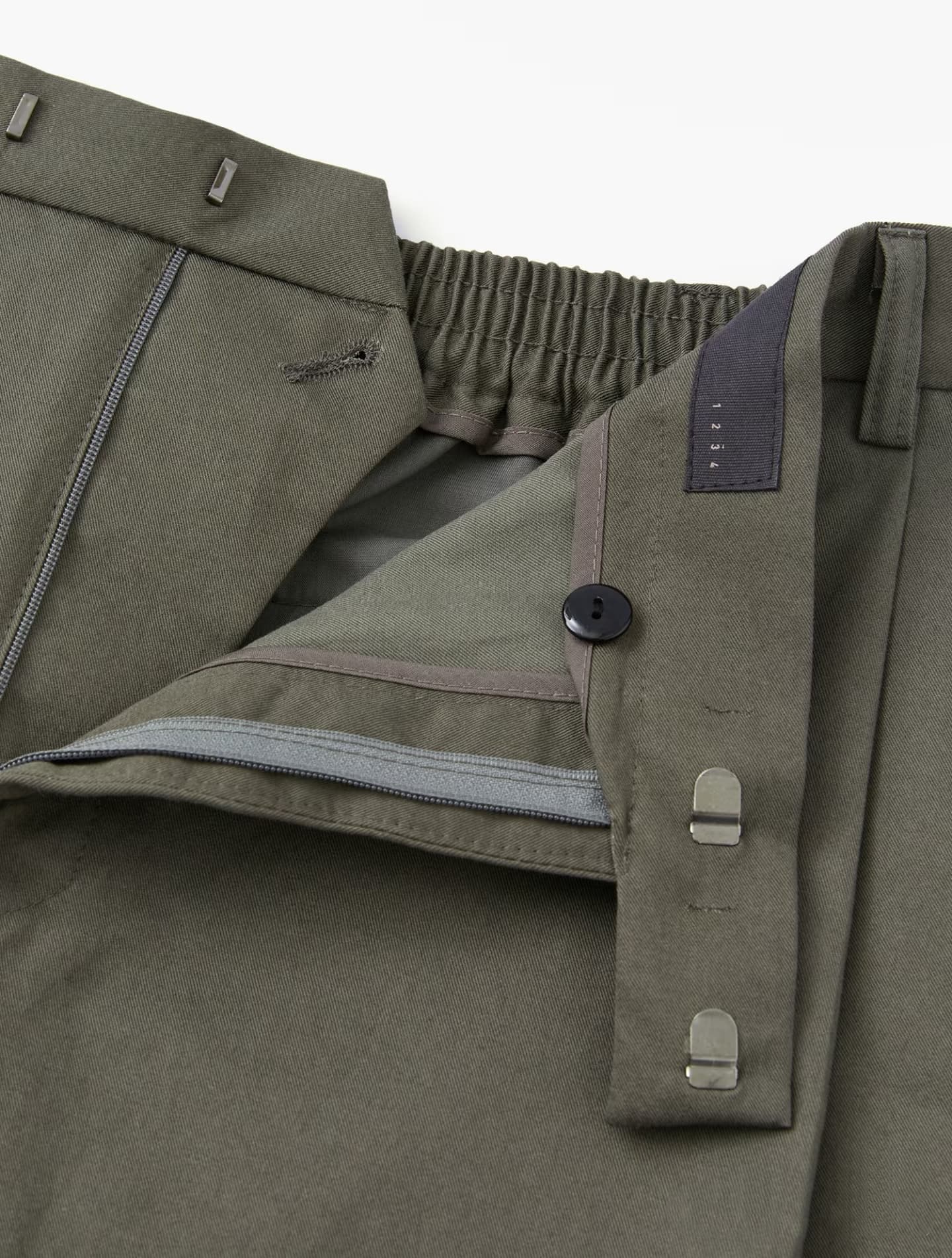 Open olive green trousers showing zipper fly, internal button, and double metal hook closures.