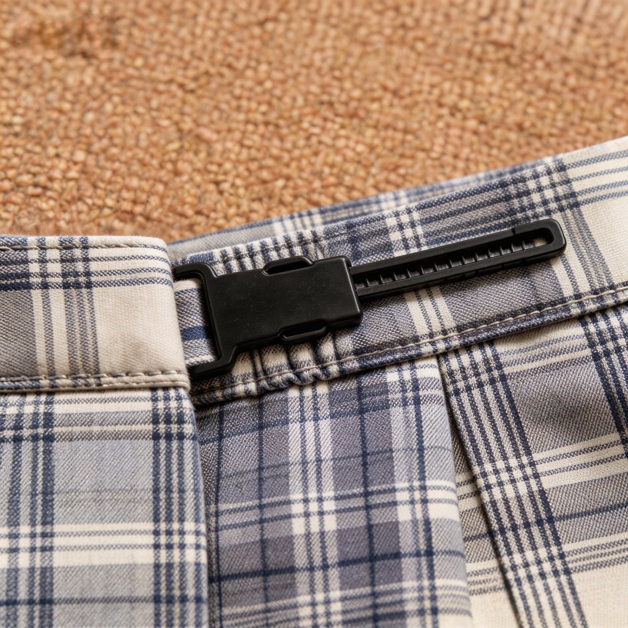 Close-up of an adjustable black plastic buckle on a blue and grey plaid skirt waistband.