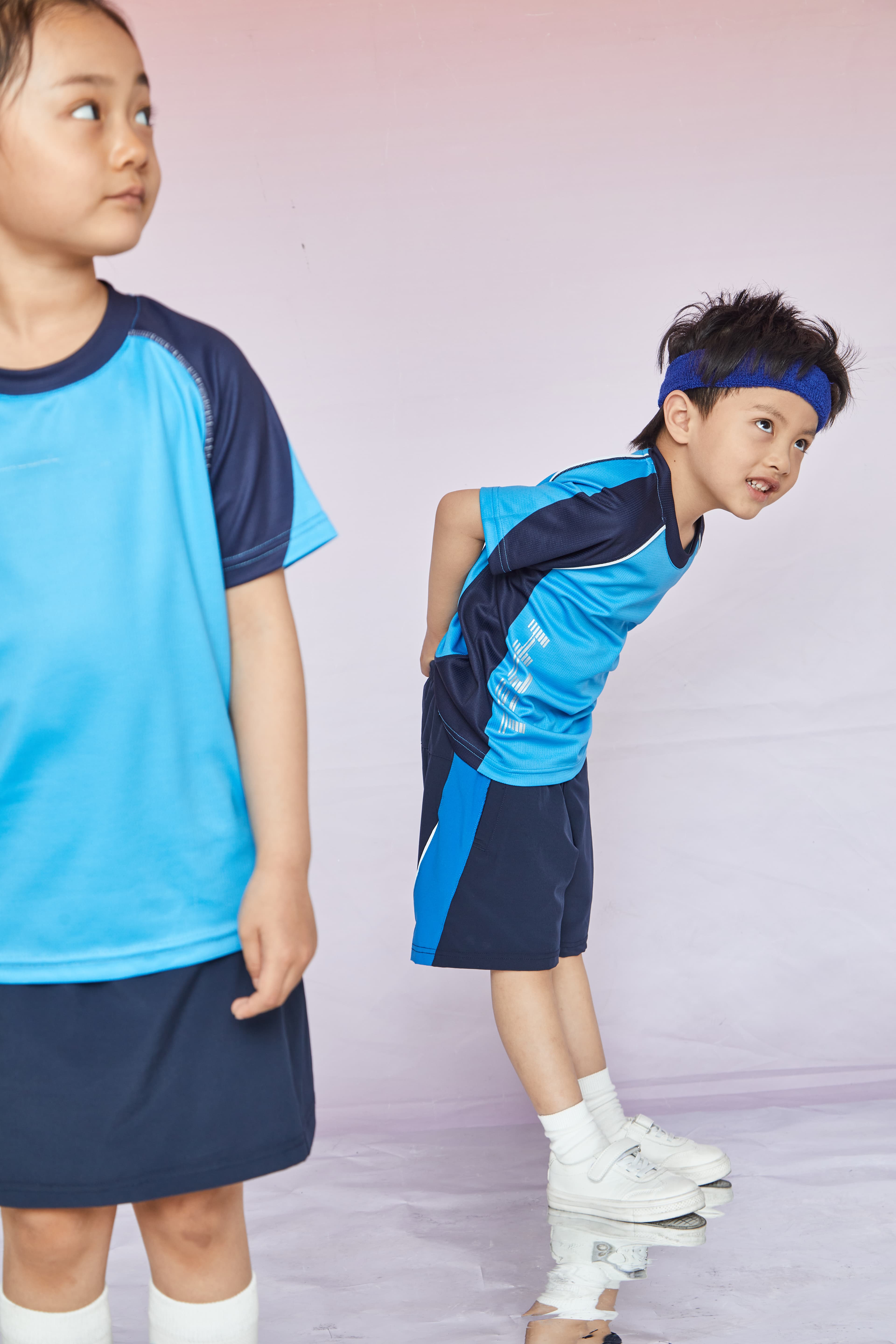 A young boy leans forward beside a girl, both wearing matching blue athletic uniforms.
