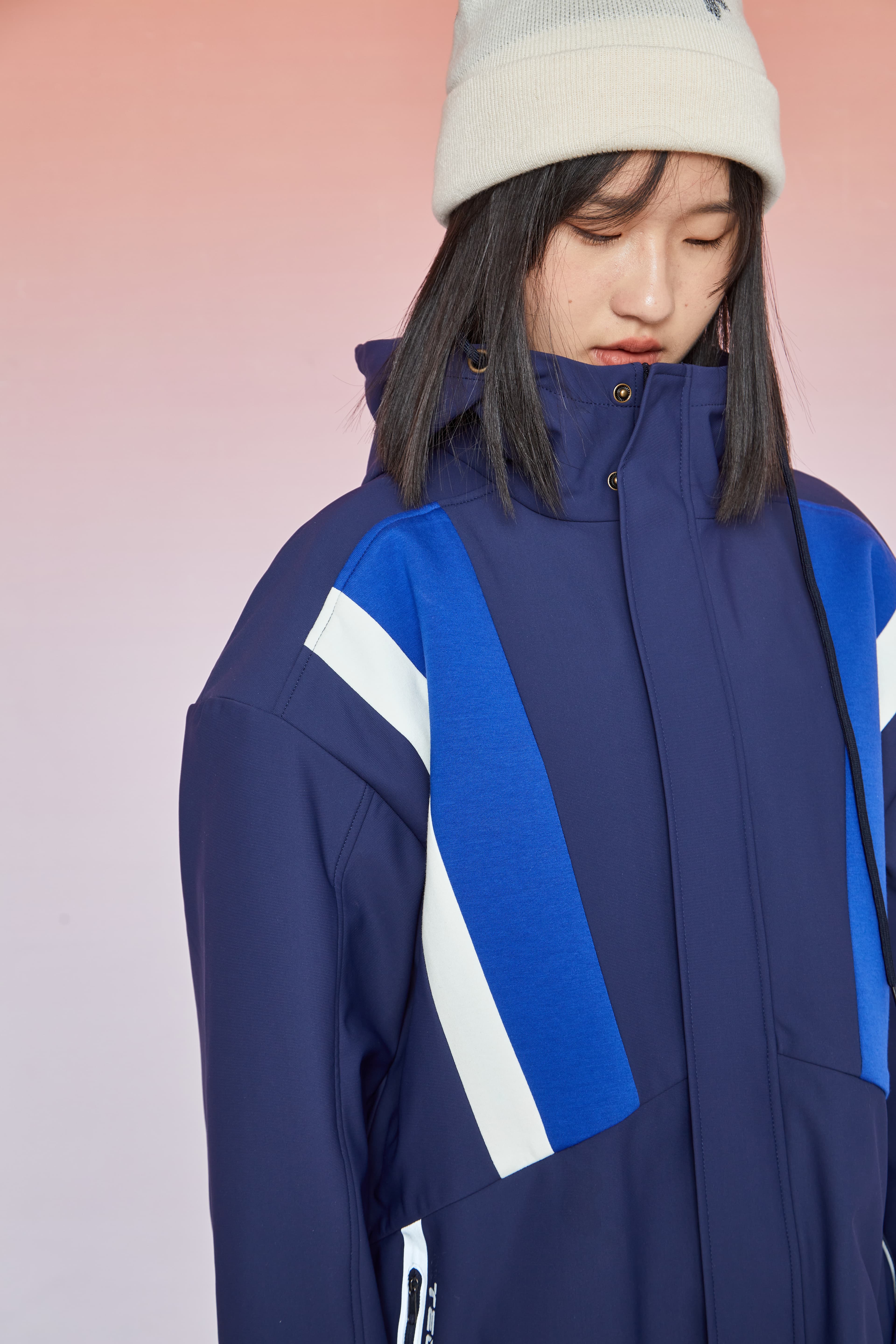 Woman in a white beanie and navy blue winter jacket with blue and white diagonal stripes.