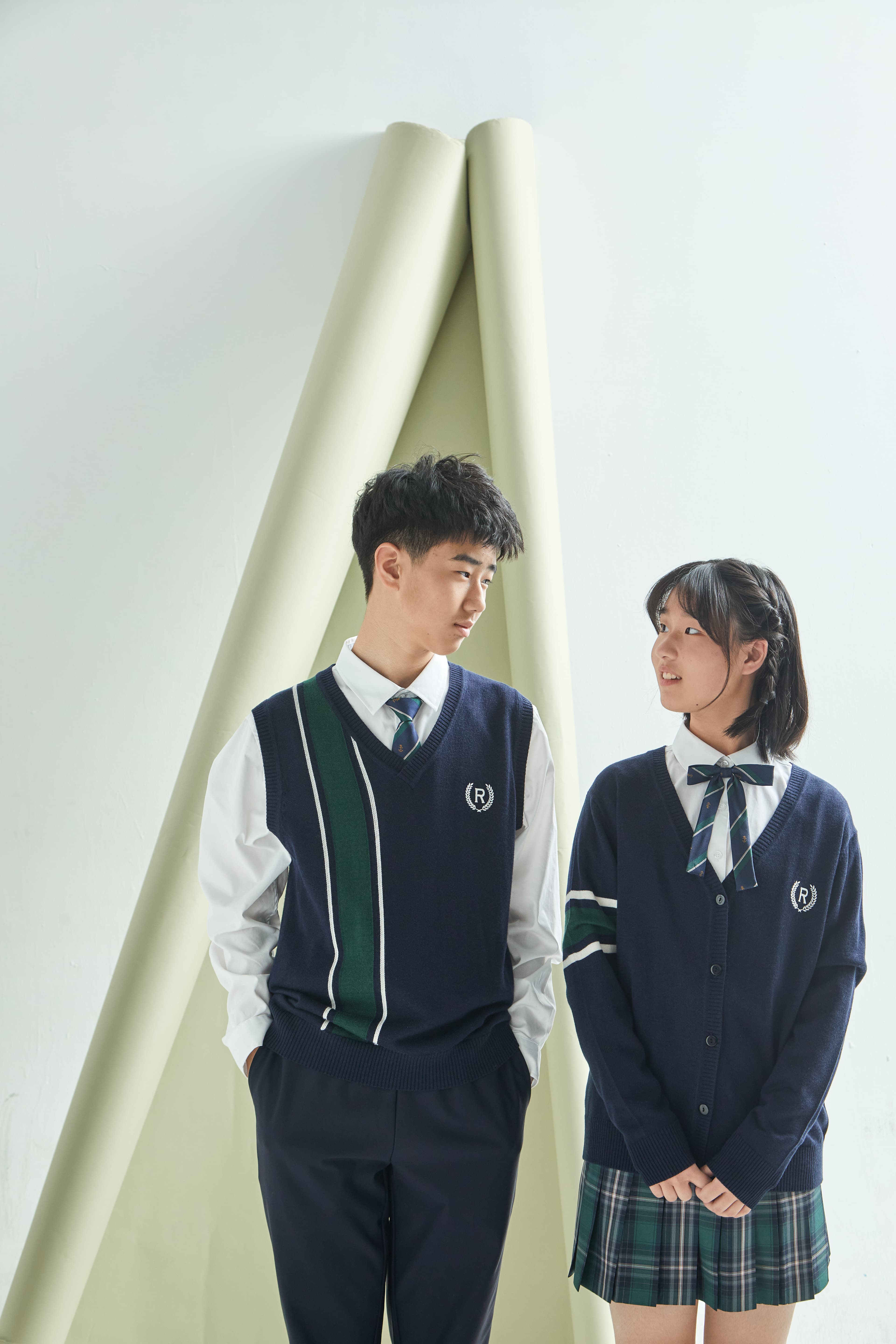 Two students in navy school uniforms look at each other against a minimalist white background.