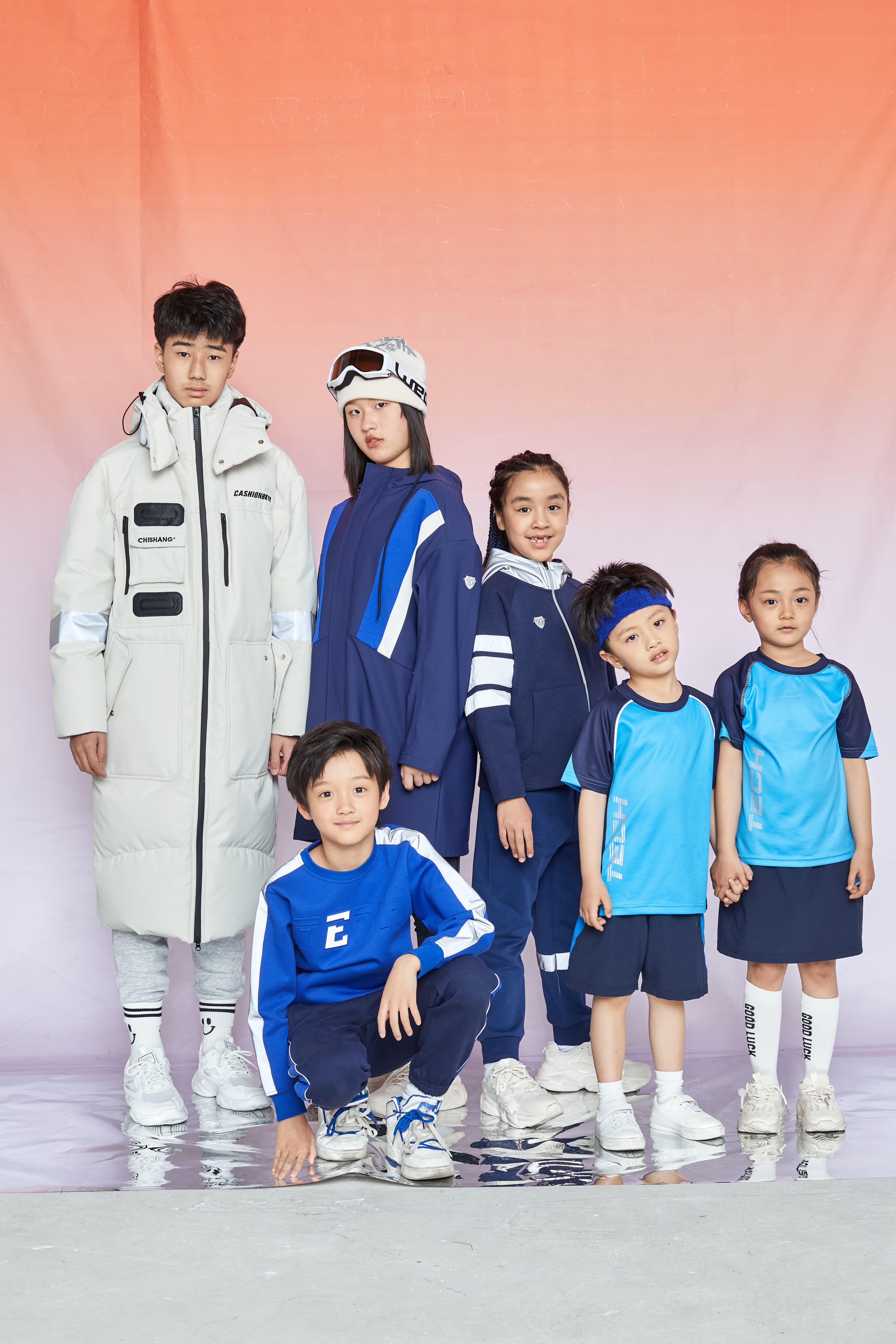 Six children in blue and white athletic and winter clothing against a pink gradient background.